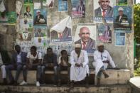 Supporters of the opposition Juwa Party sit beneath campaign posters, waiting for a rally in a village near Moroni