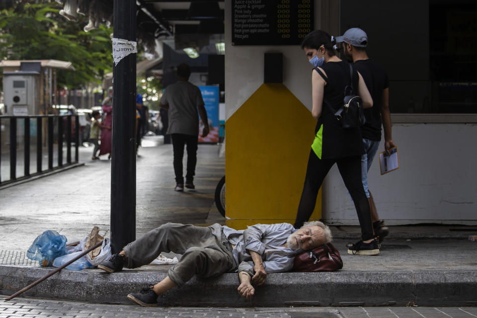 FILE - a woman looks at a homeless Lebanese man sleeping on the ground in Hamra street, in Beirut, Lebanon, July 17, 2020. The World Bank has approved a $300 million additional financing to the poor in Lebanon in which families that live in poverty will get cash payments to help them through the country's historic economic meltdown, the World Bank said in a statement released Friday, May 26, 2023. (AP Photo/Hassan Ammar, File)