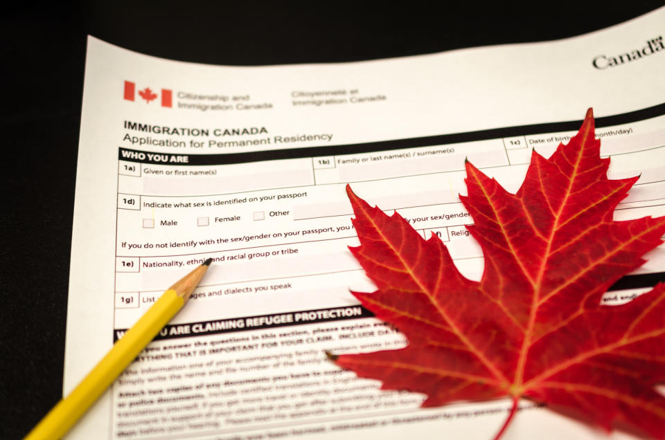 Canadian Immigration application form for permanent residency with a maple leaf and pencil placed on top