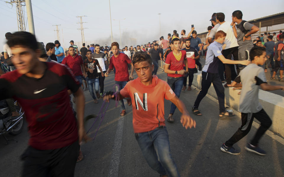Protesters run to cover from teargas fired by Israeli soldiers during a protest at the entrance of Erez border crossing between Gaza and Israel, in the northern Gaza Strip, Tuesday, Sept. 4, 2018. The Health Ministry in Gaza says several Palestinians were wounded by Israeli fire as they protested near the territory's main personnel crossing with Israel. (AP Photo/Adel Hana)