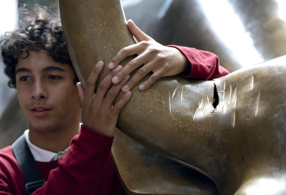 A visitor at the popular lower Manhattan sculpture "Charging Bull" poses for a photo next to the sculpture's damaged horn Sunday, Sept. 12, 2019, in New York. A man was arrested Saturday afternoon for damaging the iconic Wall Street Charging Bull statue with an object resembling a banjo, local media reported. (AP Photo/Craig Ruttle)