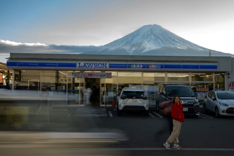 Una turista posa frente a una tienda de conveniencia sobre la que se eleva la silueta del monte Fuji en el pueblo japonés de Fujikawaguchiko, el 1 de enero de 2024 (Philip FONG)