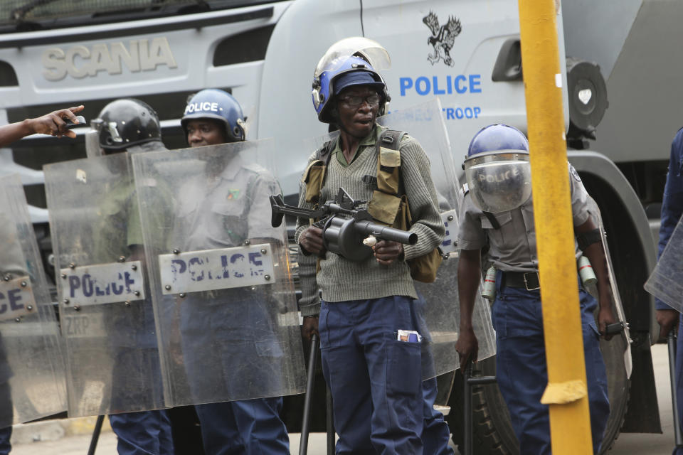 Police officers stand by near opposition party supporters who gathered to hear a speech by the country's top opposition leader in Harare, Wednesday, Nov, 20, 2019. Zimbabwean police with riot gear fired tear gas and struck people who had gathered at the opposition party headquarters to hear a speech by the main opposition leader Nelson Chamisa who still disputes his narrow loss to Zimbabwean President Emmerson Mnangagwa. (AP Photo/Tsvangirayi Mukwazhi)