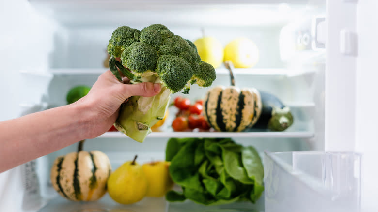 person putting broccoli in fridge