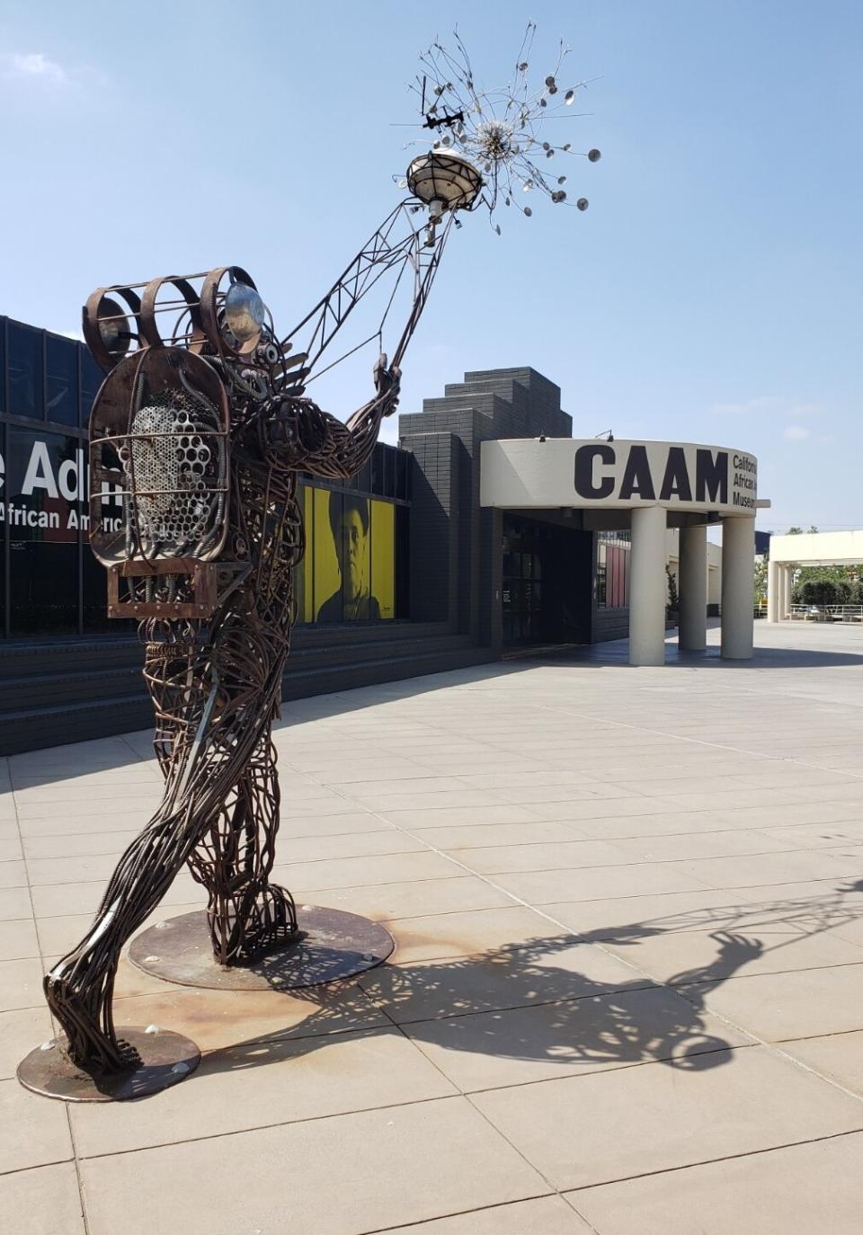 A outdoor rebar sculpture of a person pointing a divining rod toward a starburst