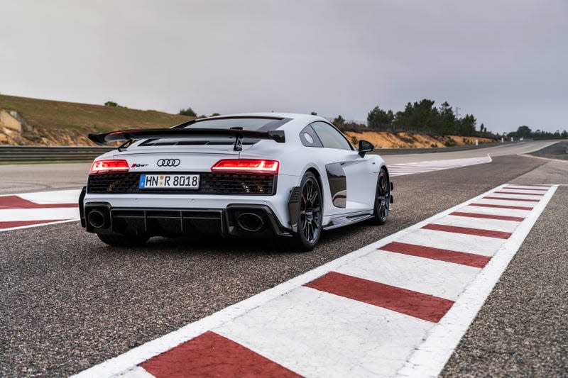 2023 audi r8 gt in grey parked on a race track, seen from the rear, with red and white striped curbing on either side of the car and a dusky sky in the background