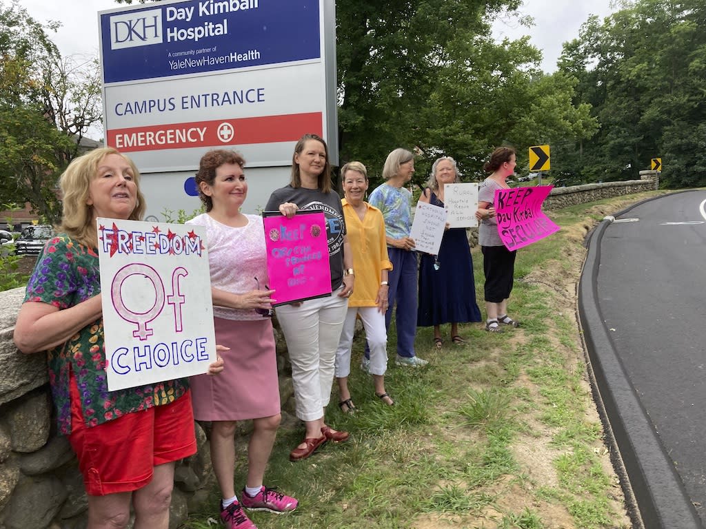 People with homemade signs standing in protest in front of a health care center.