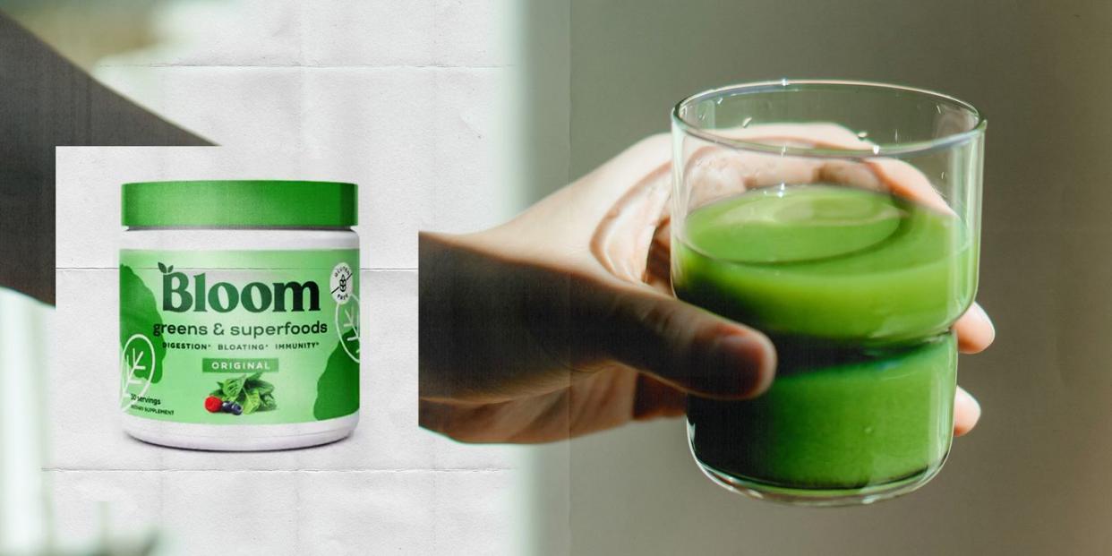 a hand holding a glass of green liquid next to a tub of bloom greens and superfoods