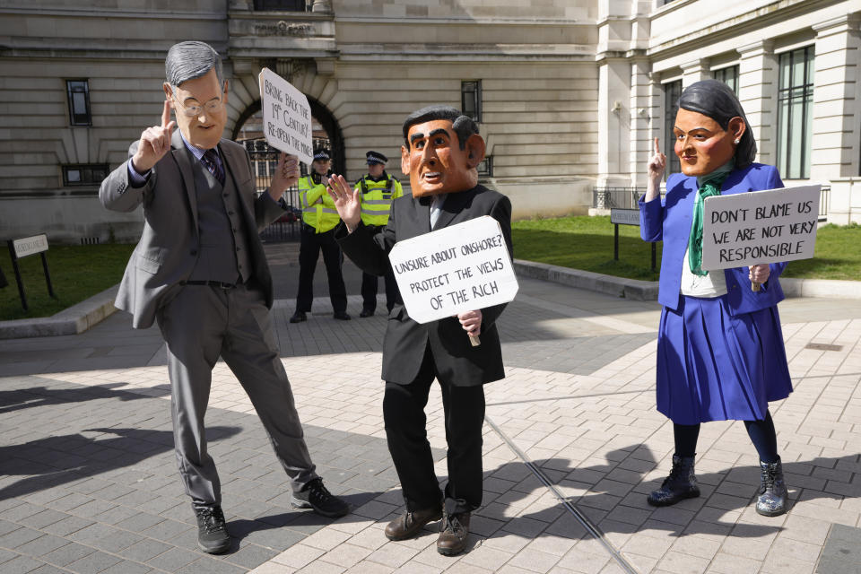Climate demonstrators dressed as Britain's politicians Jacob Rees-Mogg, Minister for Brexit Opportunities and Government Efficiency, left, Chancellor Rishi Sunak, centre, and Home Secretary Priti Patel, right, hold up placards outside the Natural History Museum as Extinction Rebellion continues a week of action and outreach in London, Monday, April 11, 2022. (AP Photo/Kirsty Wigglesworth)