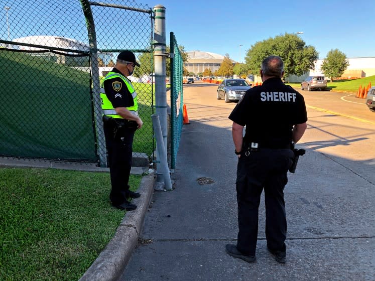 HOUSTON, TX - OCT 31, 2020 - Harris County Sheriif's Deputy R. Hilz, right, and Houston Police Officer T. Jones (left) direct traffic Friday at a Houston stadium parking lot drive by polling place and drop site for mailed ballots. (Molly Hennessy-Fiske / Los Angeles Times)