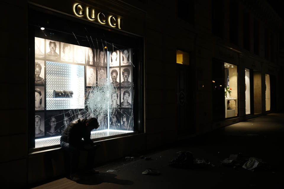 A man sits near a window broken by protesters after a demonstration near Concorde square, in Paris, Thursday, March 16, 2023. French President Emmanuel Macron has shunned parliament and imposed a highly unpopular change to the nation's pension system, raising the retirement age from 62 to 64. (AP Photo/Lewis Joly)