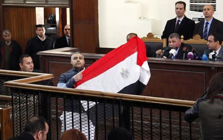 Al Jazeera journalist Mohamed Fahmy raises an Egyptian national flag while talking to the judge during his retrial at a court in Cairo February 12, 2015. REUTERS/Asmaa Waguih