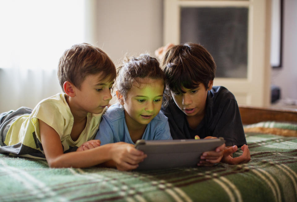 Children using a digital tablet, lying on bed, in daylight