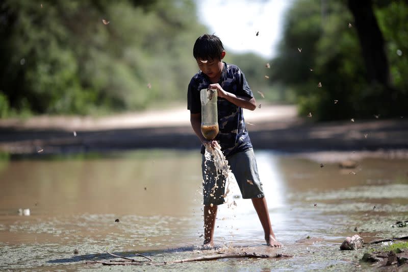 A child of the indigenous Wichi community plays with water and a plastic bottle, in the Salta province