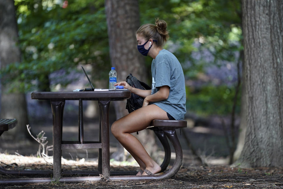 FILE - In this Aug. 18, 2020, file photo, a student works outside Ehrighaus dormitory on campus at the University of North Carolina in Chapel Hill, N.C. As more and more schools and businesses around the country get the OK to reopen, some college towns are moving in the opposite direction because of too much partying and too many COVID-19 infections among students. (AP Photo/Gerry Broome, File)