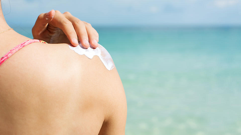 Picture of a person putting on sunscreen at the beach, while looking out to the ocean