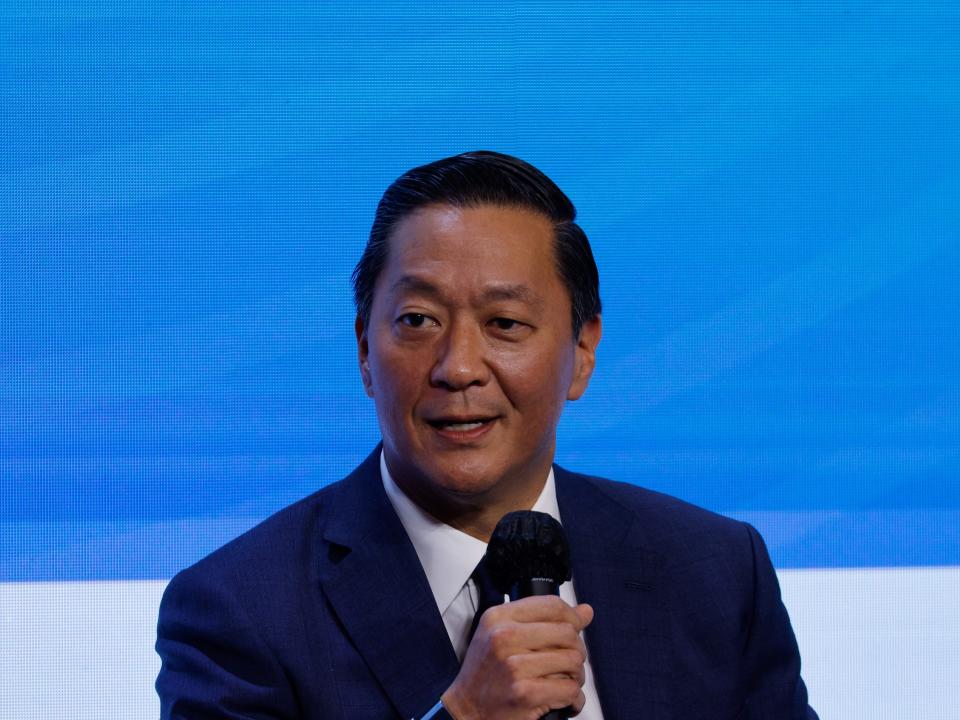Joseph Bae, the co-CEO of private equity giant KKR, sits in front of a blue background and holds a microphone.