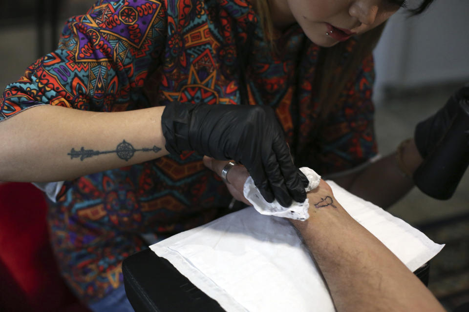 In this Saturday, 9, 2019, photo, Suraya Shaheedi, 26, Tattoo artist, left, pierced tattoo to a male customer in Kabul, Afghanistan. It’s been 18 months since Shaheedi started her mobile tattoo shop in the capital, Kabul. She’s received death threats for taking on the taboo of the ink-on-skin drawings she does — as well as being a single woman willing to work with men. (AP Photo/Rahmat Gul)