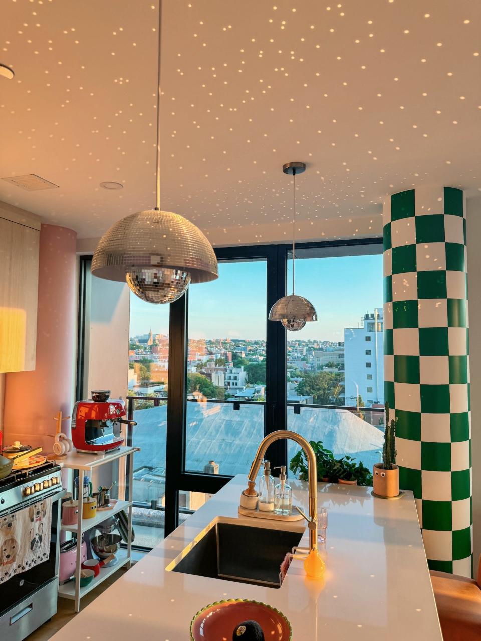 A kitchen with disco ball lights hanging from the ceiling. A pillar nearby is painted checked green and white.