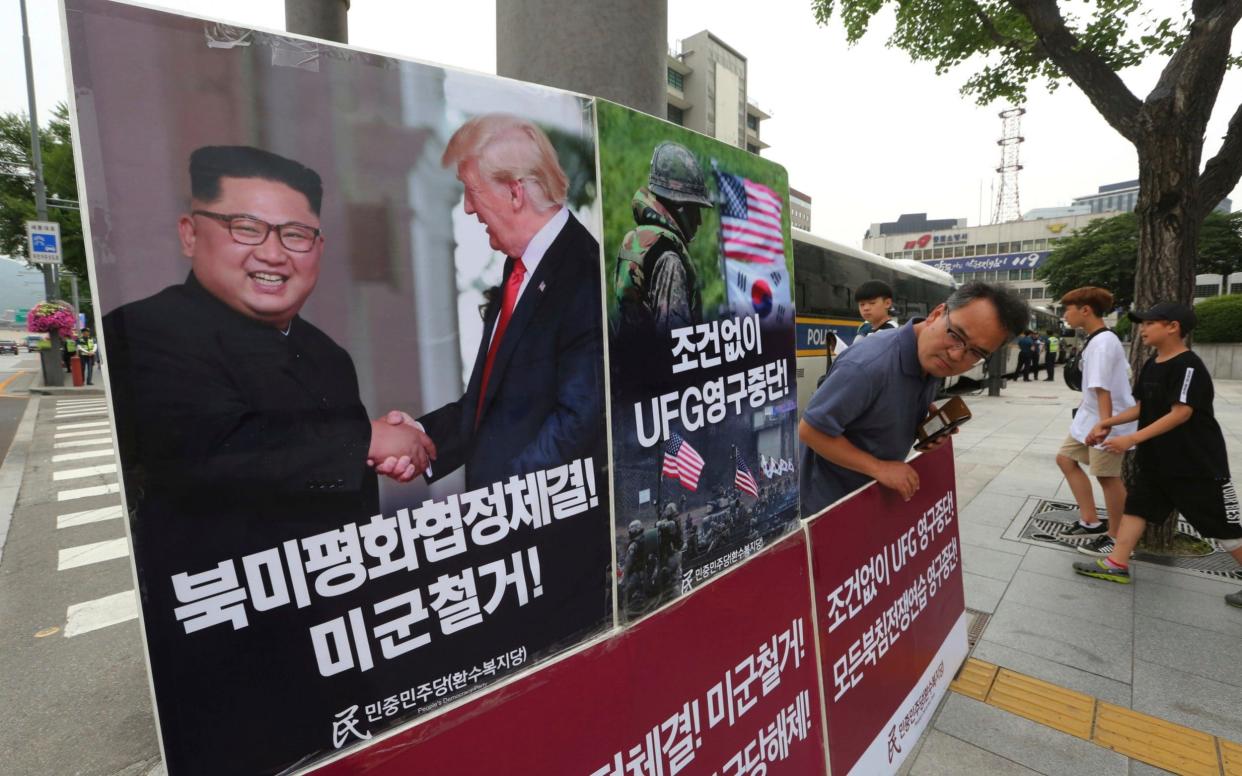 A photo showing President Donald Trump and North Korean leader Kim Jong-un is displayed as a member of the People's Democratic Party protests against military exercises between the United States and South Korea in Seoul - AP