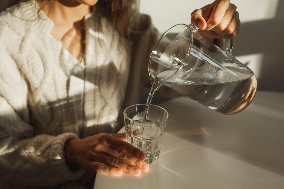 Healthy lifestyle. Young pretty smiling lady drinking water before breakfast. Morning routine. Beautiful sunlight in kitchen. Awakening. Unknown person.