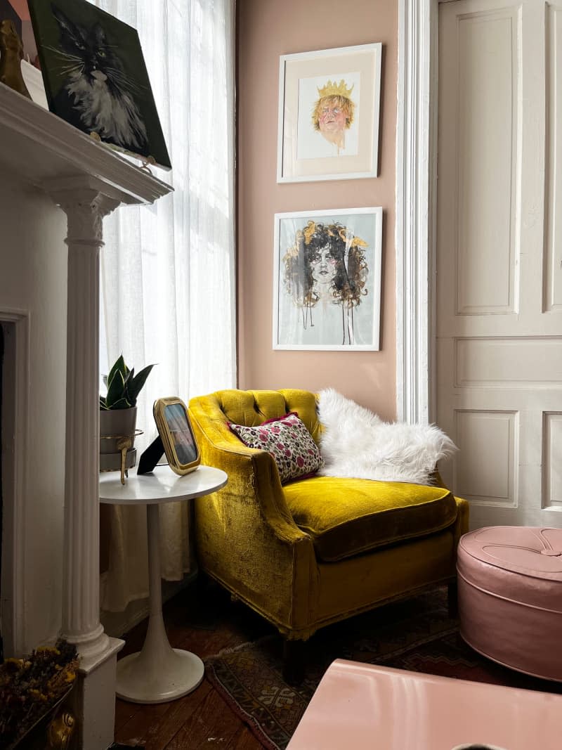 Gold velvet chair next to accept tulip table in corner of pink living room under artwork.