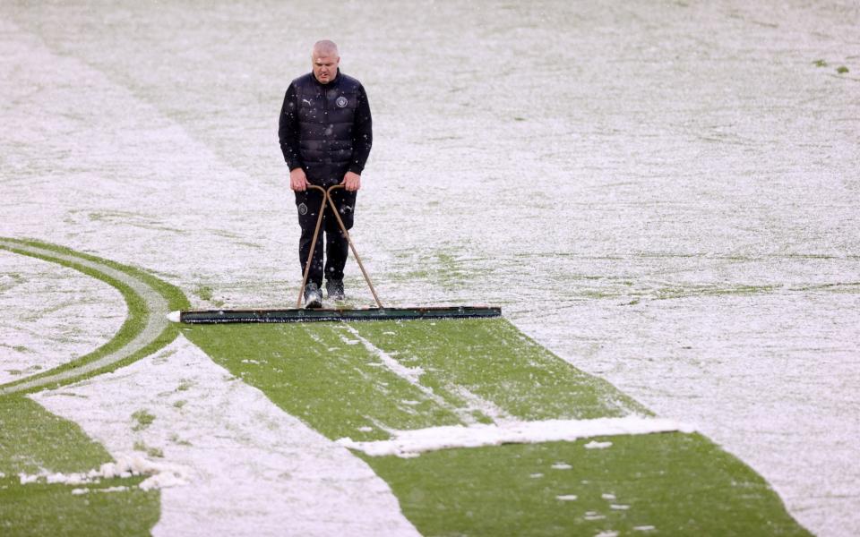  A member of ground staff is seen clearing snow from the pitch at half time during the Premier League match between Manchester City and West Ham United - Getty Images Europe 