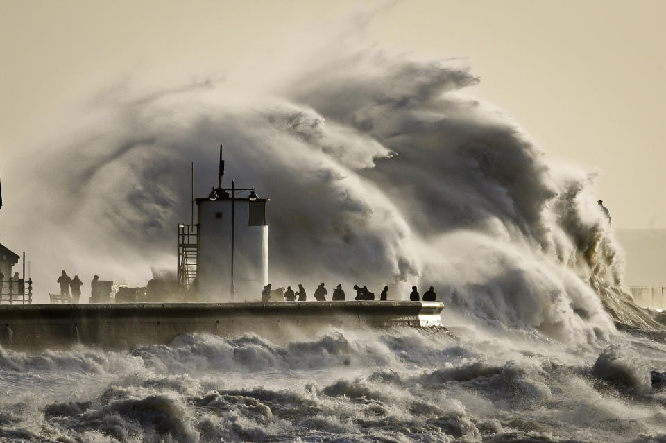 People watch and photograph enormous waves as they break, on Porthcawl harbour, South Wales, Monday Jan. 6, 2014. Residents along Britain's coasts are braced for more flooding as strong winds, rain and high tides lash the country. At least three people have died in a wave of stormy weather that has battered Britain since last week, including a man killed when his mobility scooter fell into a river in Oxford, southern England. (AP Photo/PA, Ben Birchall) UNITED KINGDOM OUT