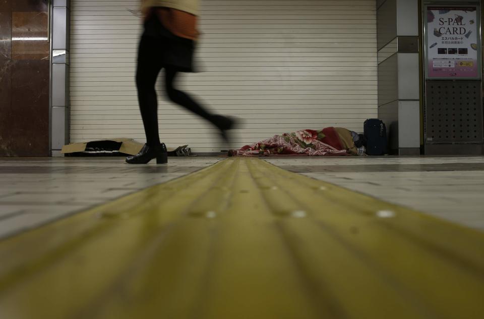 Shizuya Nishiyama (R), a 57-year-old homeless man from Hokkaido, and an another homeless man sleep on the ground as a passerby walks past at a concourse of Sendai Station in Sendai, northern Japan December 18, 2013. (REUTERS/Issei Kato)