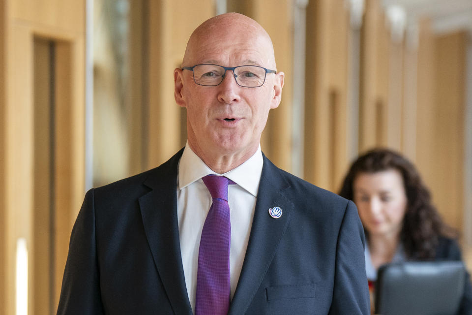 John Swinney smiles for the camera as he walks to First Minister's Questions.