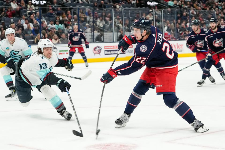 Jan 13, 2024; Columbus, Ohio, USA; Columbus Blue Jackets defenseman Jake Bean (22) shoots past Seattle Kraken left wing Brandon Tanev (13) during the third period of the NHL hockey game at Nationwide Arena. The Blue Jackets lost 7-4.