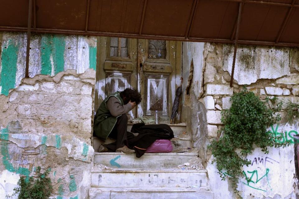 A homeless person sits at the entrance of an abandoned house in central Athens, during one of the coldest days of this winter on Wednesday, Feb. 29, 2012. Late Tuesday, parliament approved new cuts in public sector pensions and government spending required to secure a second package of international rescue loans, while the Cabinet formally imposed deep cuts to the minimum wage, retroactively to Feb. 14.(AP Photo/Petros Giannakouris)