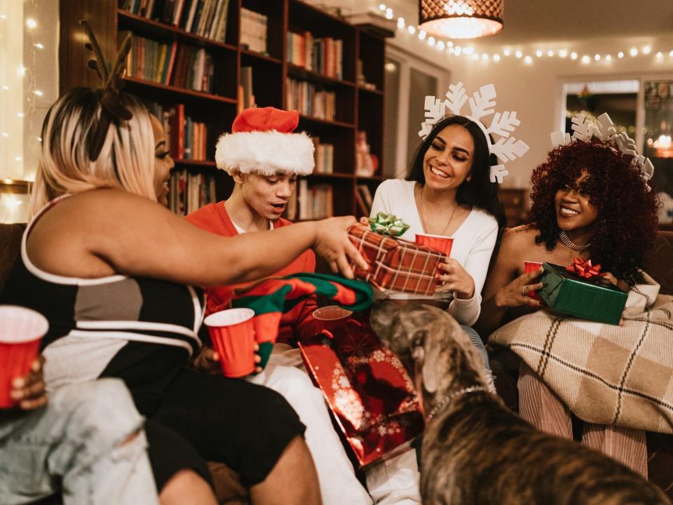 A group of friends exchange presents on a couch as a dog sniffs them.