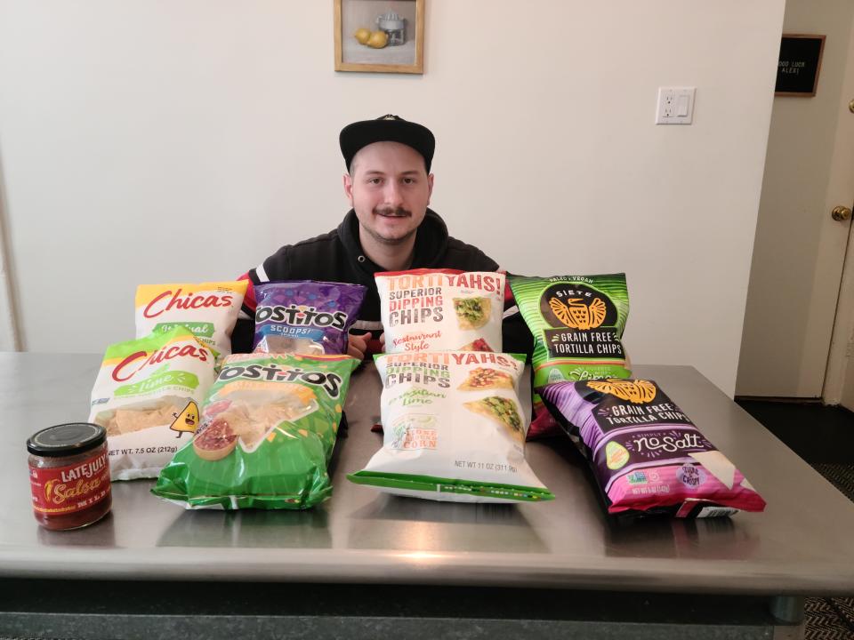 Author sitting behind eight bags of tortilla chips and one jar of salsa.