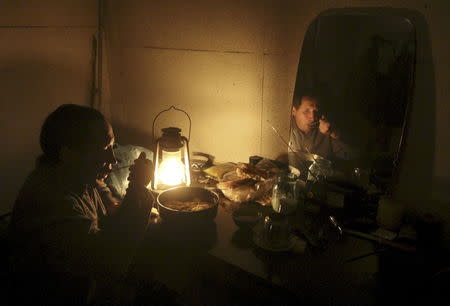 Ravshan, a Crimean Tatar, is reflected in a mirror as he eats by the light of a burning oil lamp due to a power cut inside his house in the village of Strogonovka, Simferopol district, Crimea, in this November 26, 2015 file photo. REUTERS/Pavel Rebrov/Files