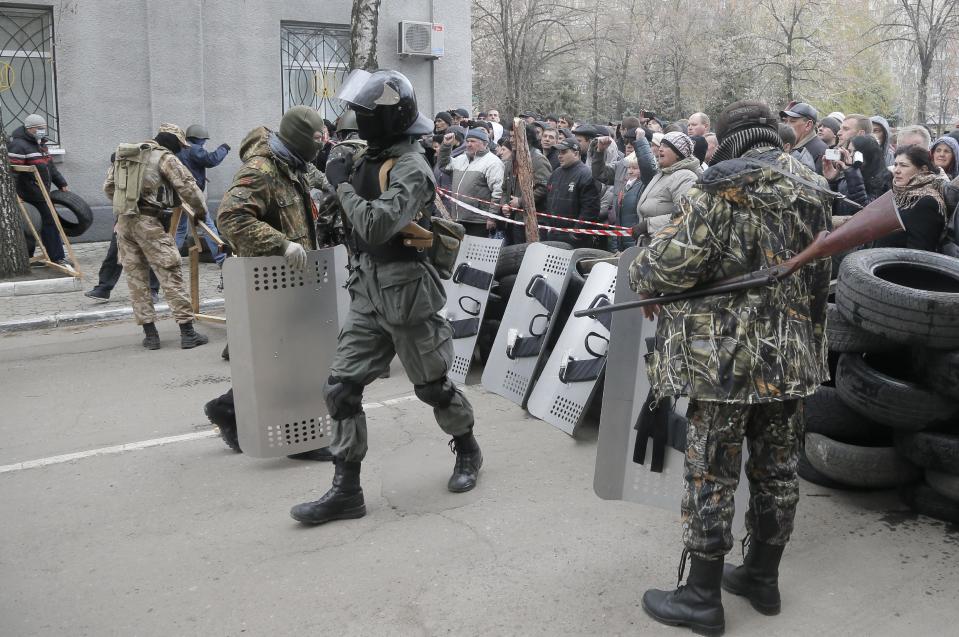 Armed pro-Russian activists occupy the police station carrying riot shields as people watch on, in the eastern Ukraine town of Slovyansk on Saturday, April 12, 2014. Pro-Moscow protesters have seized a number of government buildings in the east over the past week, undermining the authority of the interim government in the capital, Kiev. (AP Photo/Efrem Lukatsky)