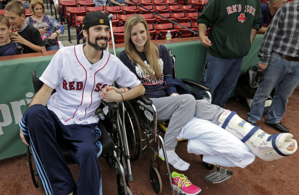 FILE - In this May 23, 2013 file photo, Boston Marathon bombing survivor Pete DiMartino, of Rochester, N.Y., and his girlfriend, Rebekah Gregory, hold hands prior to DiMartino throwing out the ceremonial first pitch before a Red Sox game at Fenway Park in Boston. DiMartino and Gregory were injured in an explosion near the finish line of the Boston Marathon. The couple were chosen for the “Dream Wedding Contest” given by Theknot.com, a wedding planning website. Gregory’s fit-and-flare Sophia Moncelli dress, the couple’s rings and location were chosen by the site’s users. The couple tied the knot last April in front of 125 people at the Biltmore Estate in Asheville, North Carolina. Her search for the perfect wedding dress is featured in Friday night’s season finale of TLC’s popular reality show, “Say Yes to the Dress.” (AP Photo/Charles Krupa, File)