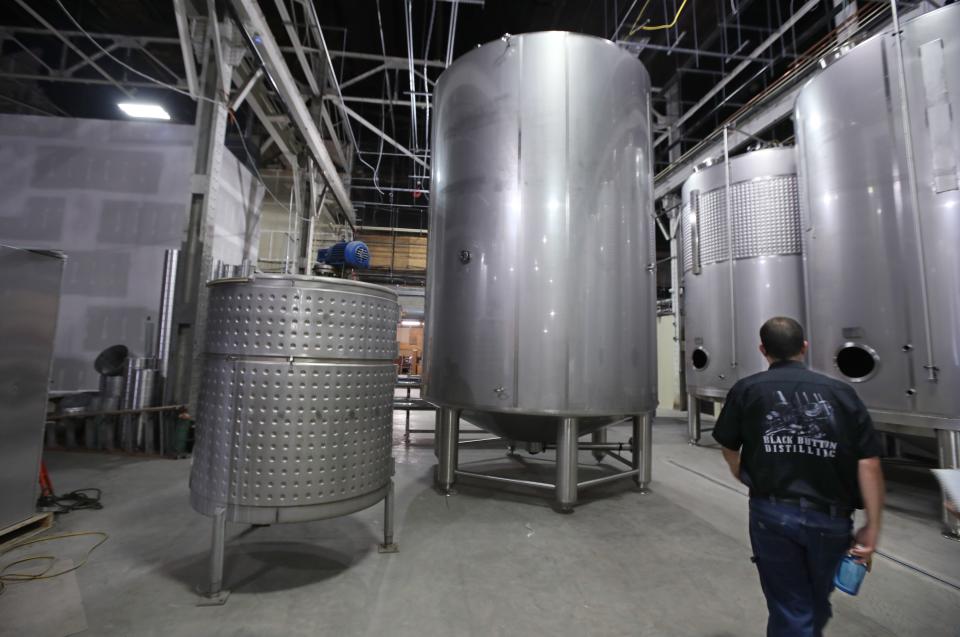 Owner Jason Barrett walks past his original mash ton tank, 600 gallons, seen at far left, in the production area at the new location of Black Button Distilling, now located at 1344 University Ave in Rochester.  The new mash ton, seen just to the right of the original, is 6,000 gallons.