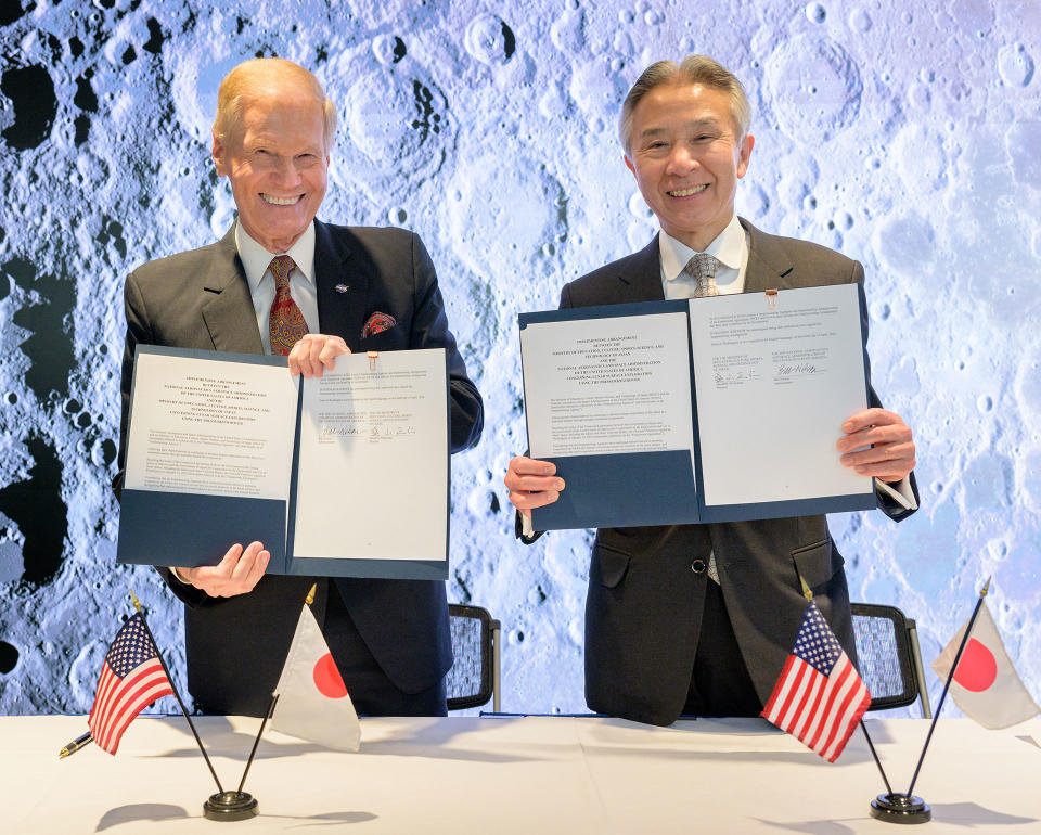 two smiling men in suits hold up signed documents to the camera