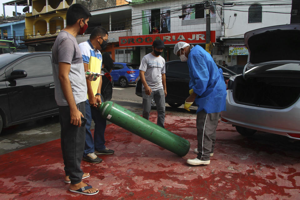 The relatives of patients with COVID-19 take an empty oxygen tank to their car which they will drive to a store to be refilled and bring back, outside the Joventina Dias Hospital in Manaus, Brazil, Friday, Jan. 15, 2021. Hospital staff and relatives of COVID-19 patients rushed to provide facilities with oxygen tanks just flown into the city as doctors chose which patients would breathe amid dwindling stocks and an effort to airlift some of them to other states. (AP Photo/Edmar Barros)