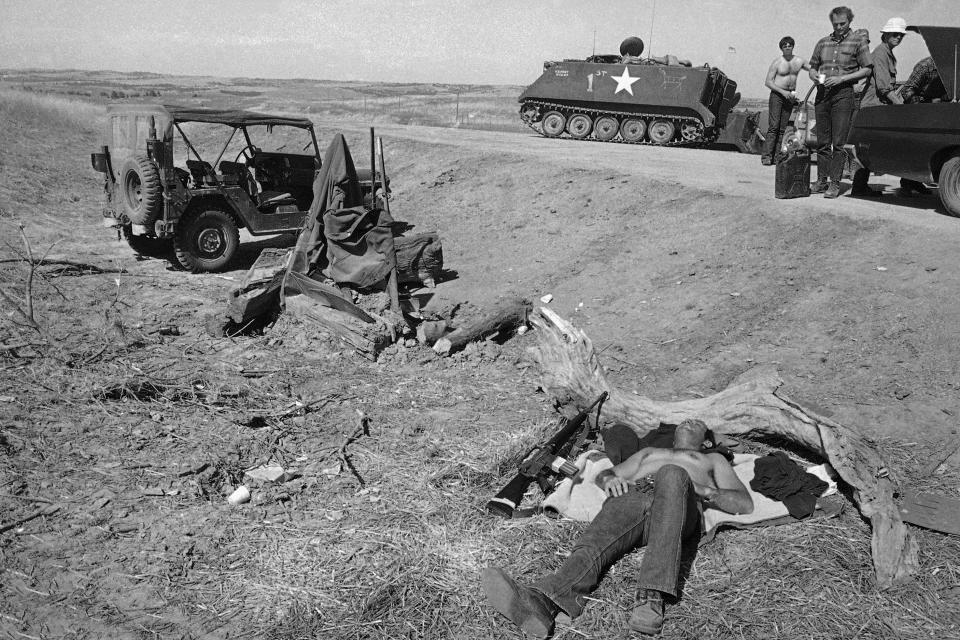 FILE - An FBI agent rests at the main roadblock into Wounded Knee, S.D., on April 29, 1973, next to his rifle, as negotiations continue to seek an end of the American Indian Movement occupation of the town. (AP Photo/Jim Mone, File)