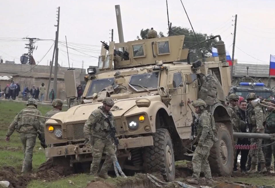 In this frame grab from video, people and soldiers gathering next to an American military convoy stuck in the village of Khirbet Ammu, east of Qamishli city, Syria, Wednesday, Feb. 12, 2020. Syrian media and activists say a Syrian was killed and another wounded in a rare clash between American troops and a group of government supporters in northeast Syria. (AP Photo)