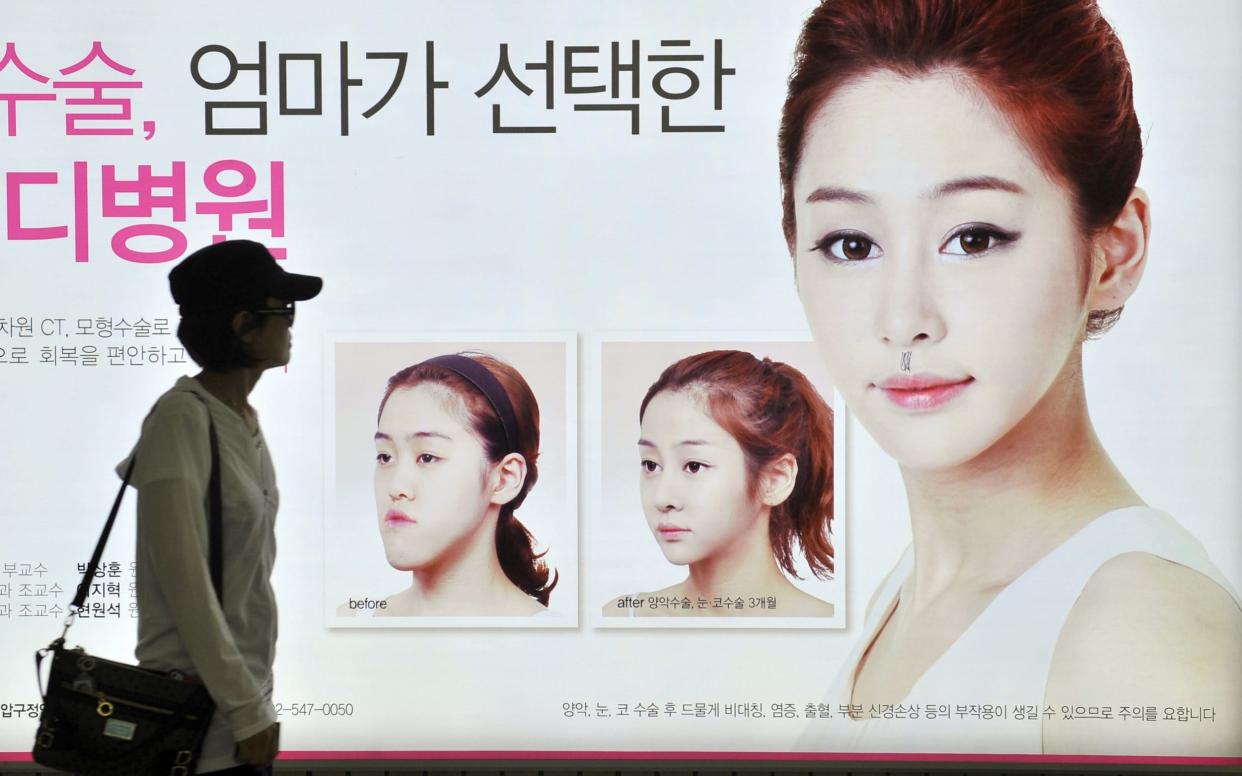 A South Korean woman walking past a street billboard advertising double-jaw surgery at a subway station in Seoul - AFP