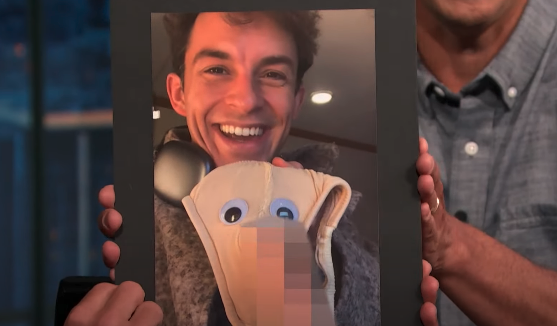 Jonathan Bailey smiles while holding a framed photo of himself with a stuffed toy