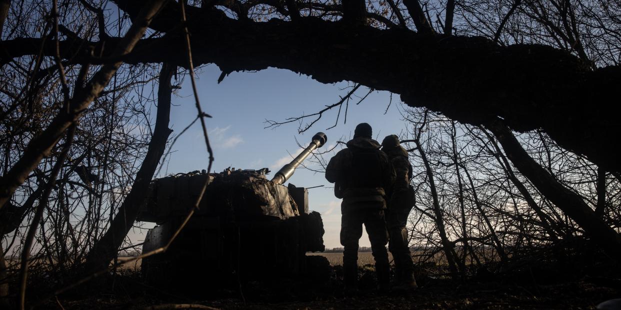 Members of a Ukrainian artillery unit stand near a artillery unit in the forest.