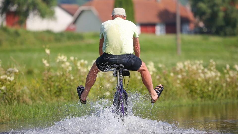 Ein Radfahrer fährt in Sandalen auf dem vom Regen überfluteten Donau-Radwanderweg durch das Hochwasser.