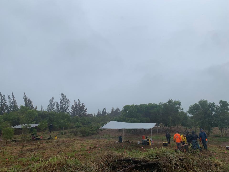 A group of people in a field with a tent on a cloudy day