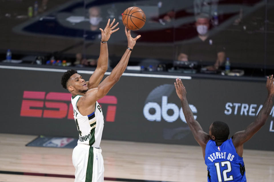 Giannis Antetokounmpo de los Bucks de Milwaukee lanza el balón superando a Gary Clarke del Magic de Orlando en el quinto juego de la serie de primera ronda de la Conferencia Este el sábado 29 de agosto del 2020 en Lake Buena Vista, Florida. (AP Photo/Ashley Landis)