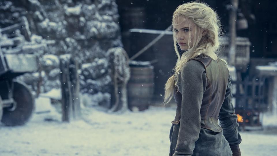 A young blonde girl stands in a snowy outdoor area in a castle