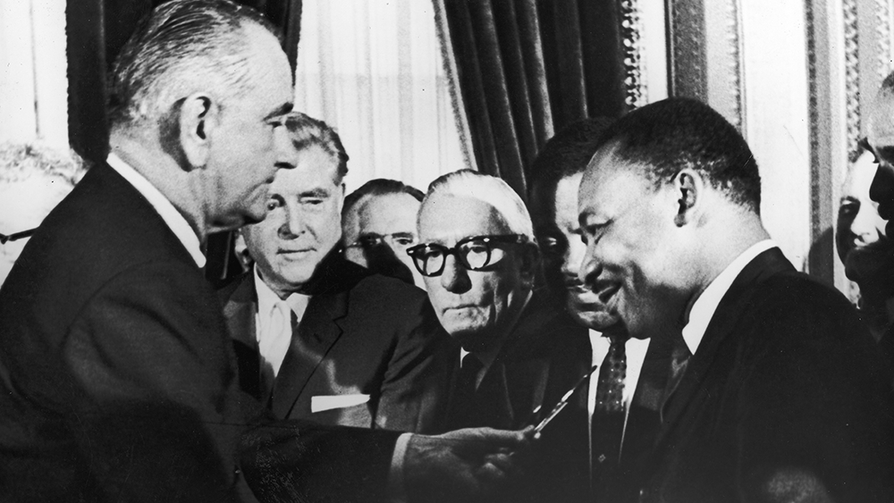 President Lyndon B Johnson hands a pen to civil rights leader Rev. Martin Luther King Jr during the signing of the Voting Rights Act as officials look on behind them, Washington D.C., August 6, 1965. (Photo by Washington Bureau/Getty Images)